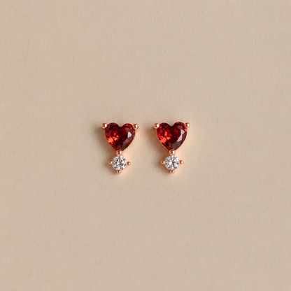 Heart-shaped red gemstone earrings with rose gold setting on a beige background