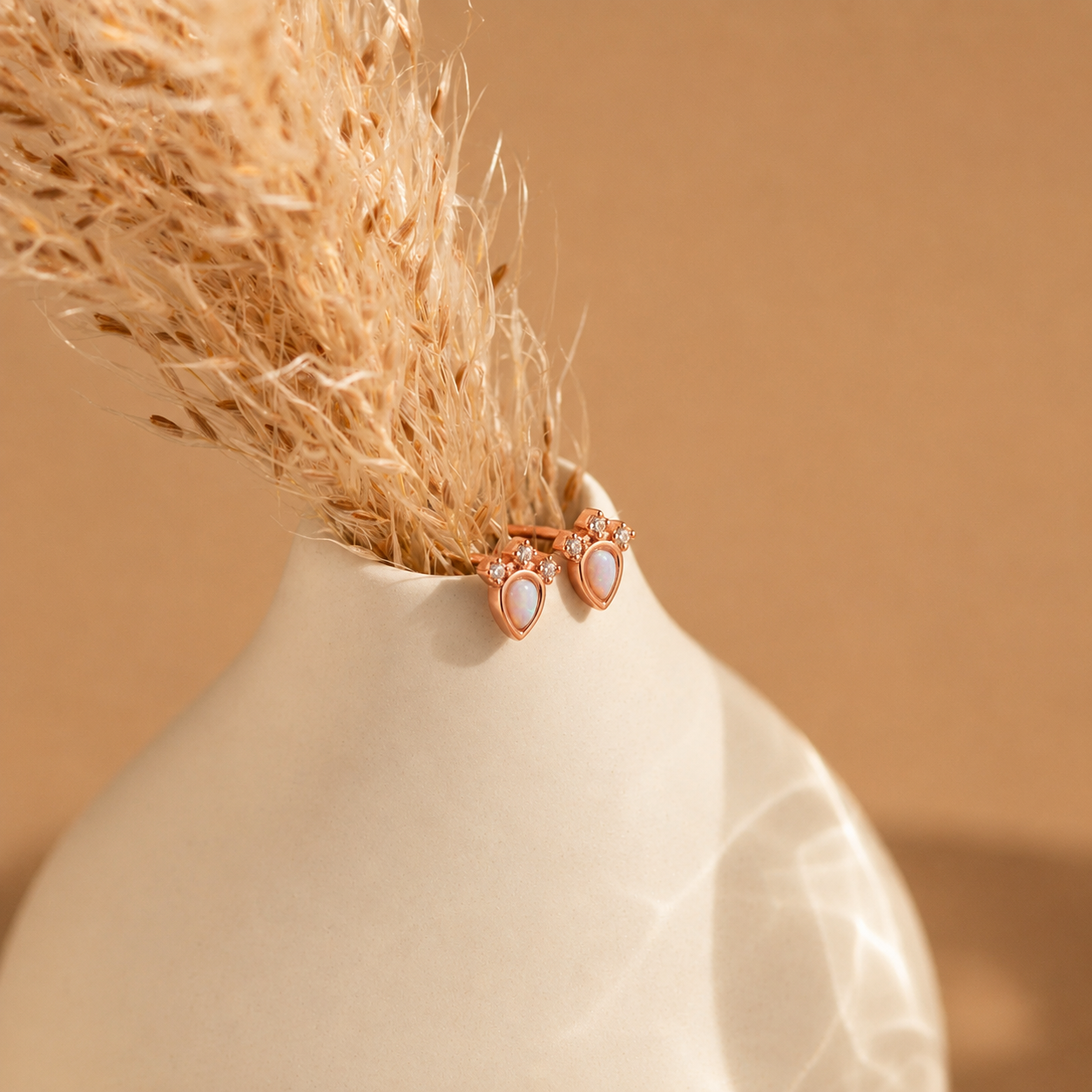 Two rose gold earrings with clear stones in a beige vase against a beige background