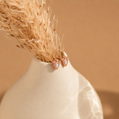 Two rose gold earrings with clear stones in a beige vase against a beige background