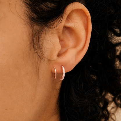 Close-up of an ear wearing rose gold hoop earrings with a blurred background