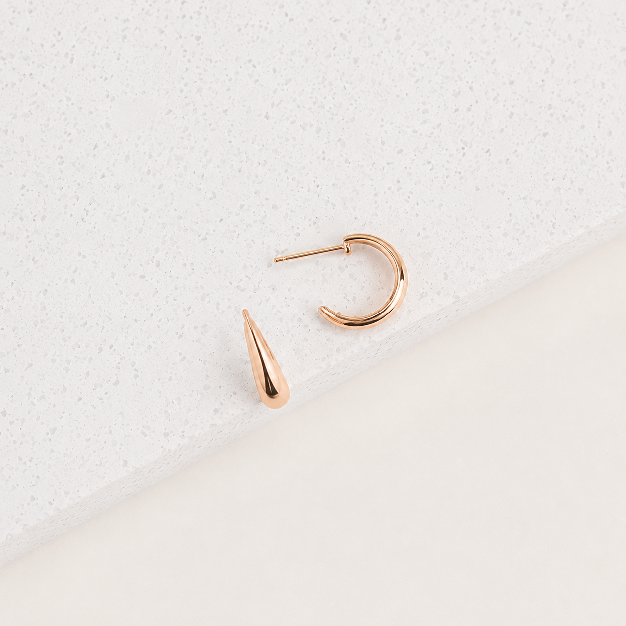 Rose gold hoop earring with a teardrop-shaped pendant on a light gray textured background