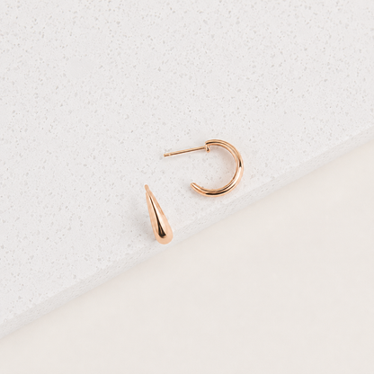 Rose gold hoop earring with a teardrop-shaped pendant on a light gray textured background