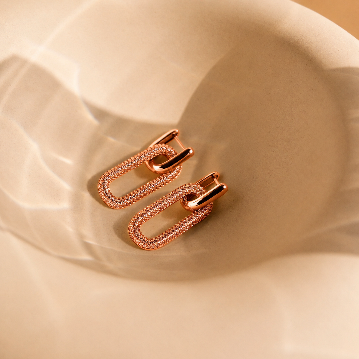 Rose gold earrings on a beige fabric background