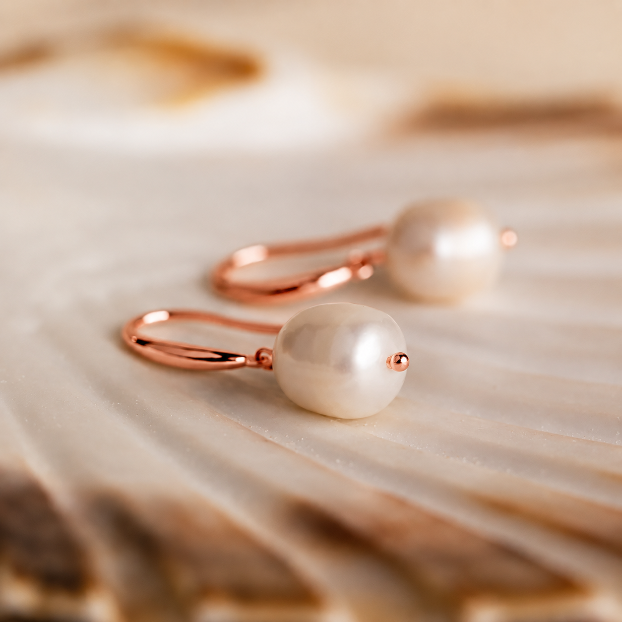 Pearl earrings with rose gold hooks on a textured beige surface