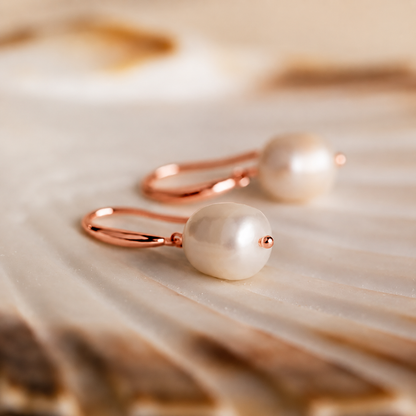 Pearl earrings with rose gold hooks on a textured beige surface