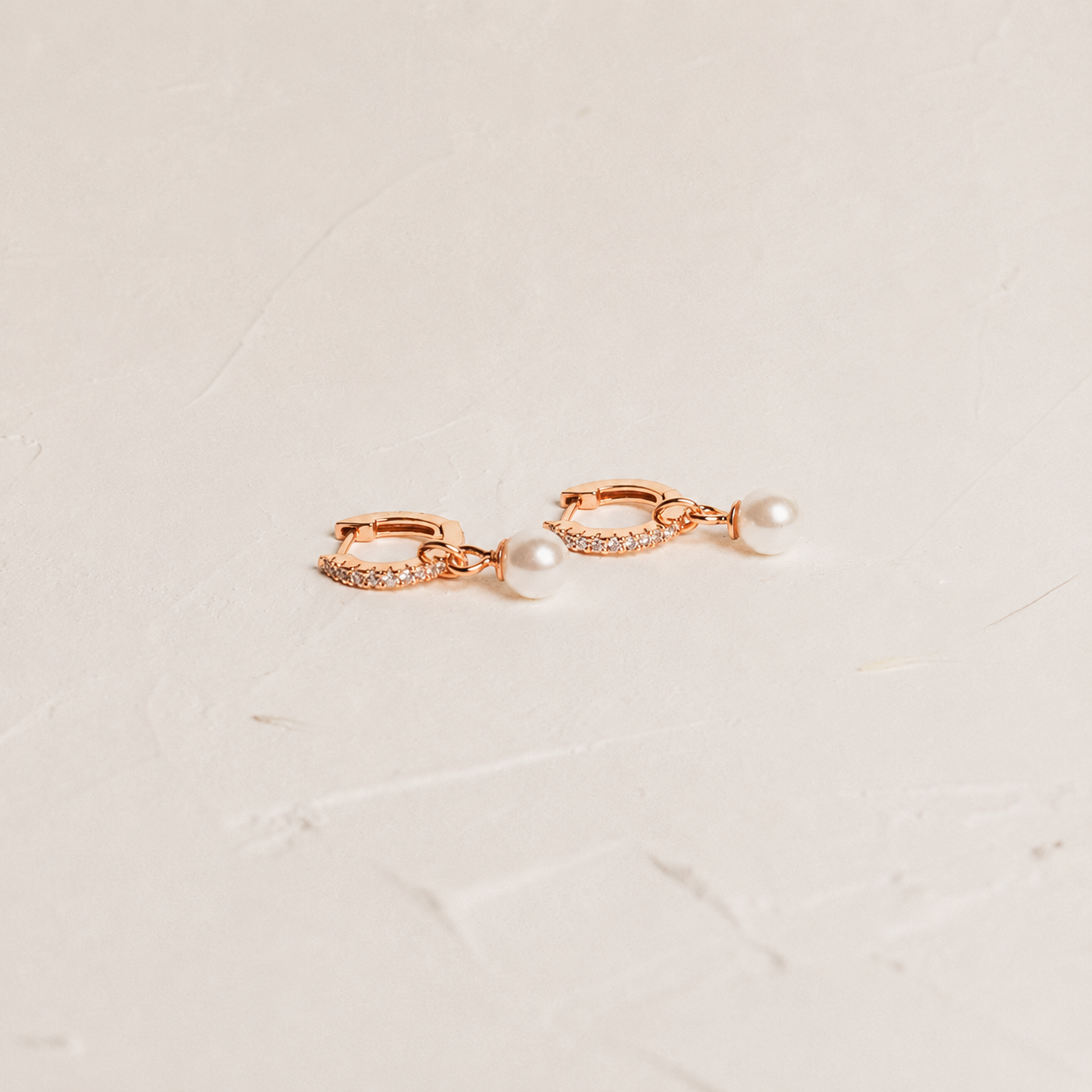 Rose gold earrings with pearls on a light beige marble background