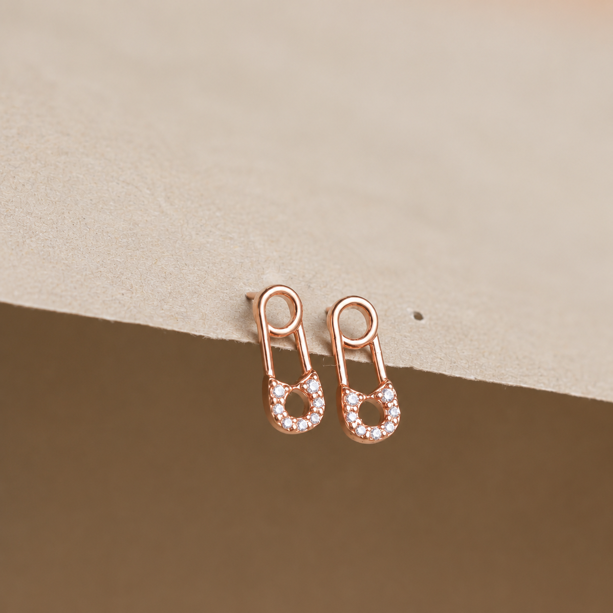 Rose gold earrings with small diamonds on a beige background