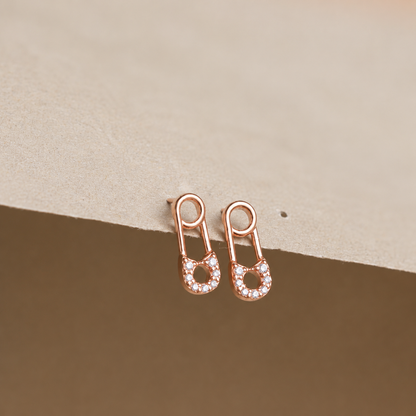 Rose gold earrings with small diamonds on a beige background