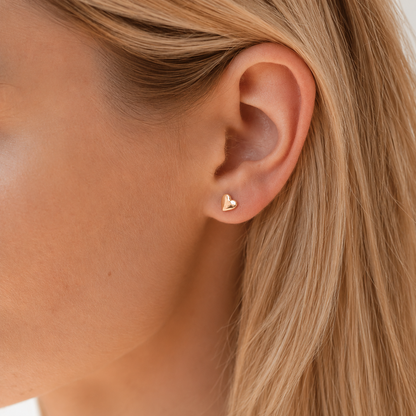 Close-up of an ear wearing a gold heart-shaped earring with blonde hair.