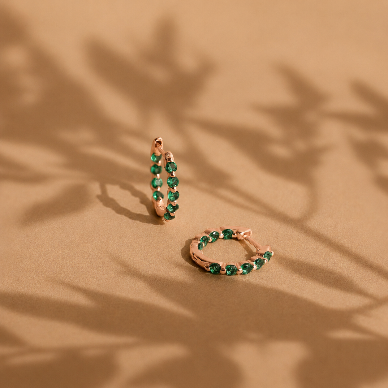 Rose gold hoop earrings with green gemstones on a beige background