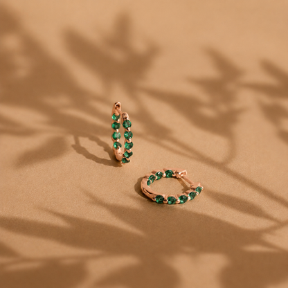 Rose gold hoop earrings with green gemstones on a beige background