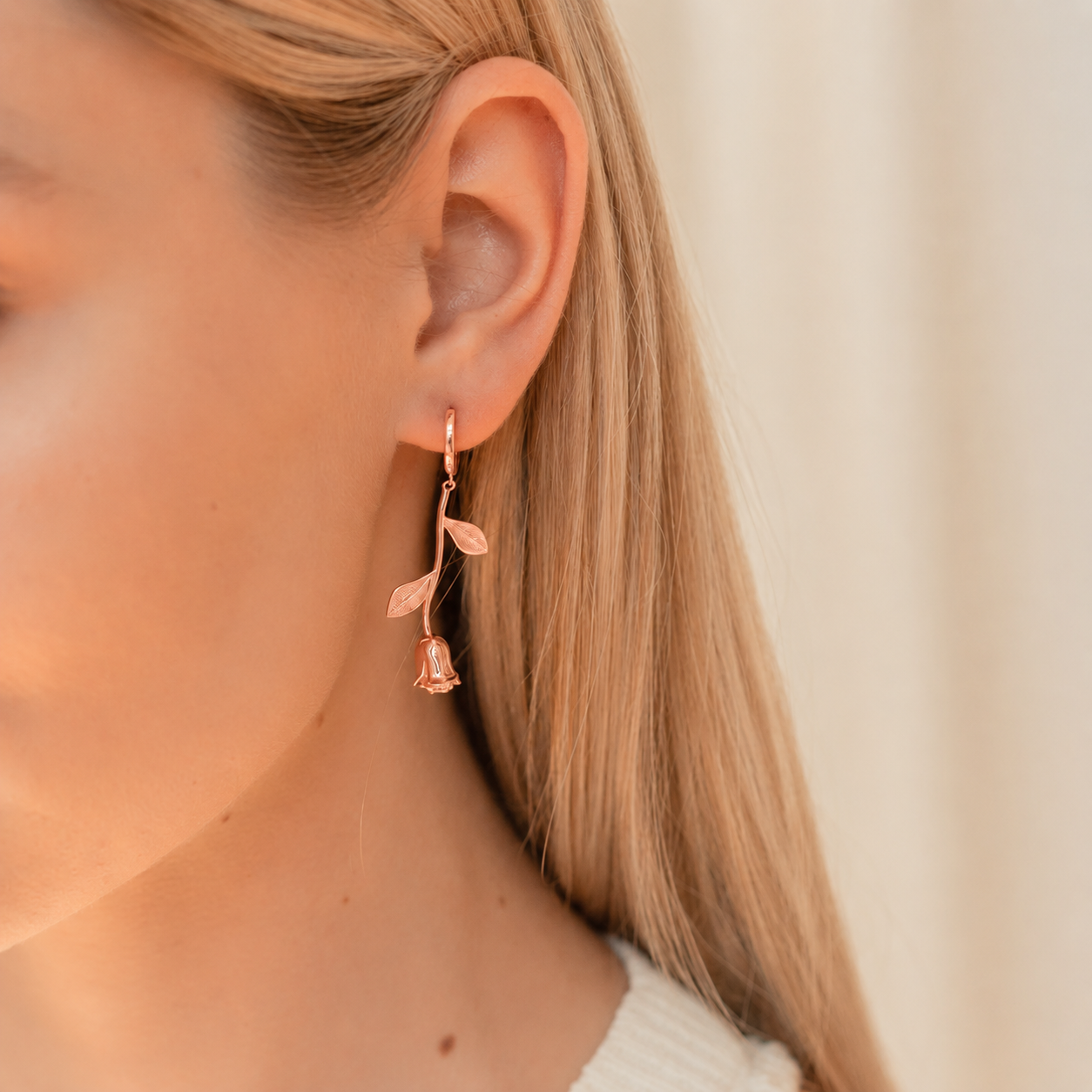 Rose gold floral earring worn by a person with blonde hair.