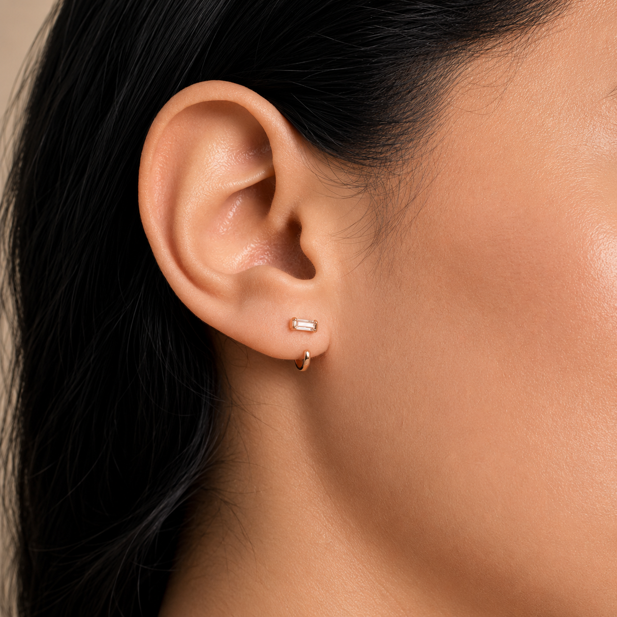 Close-up of an ear wearing a gold hoop earring with a neutral background