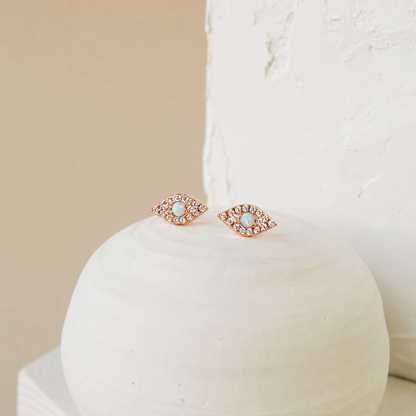 Rose gold earrings with gemstones on a white cushion against a beige background