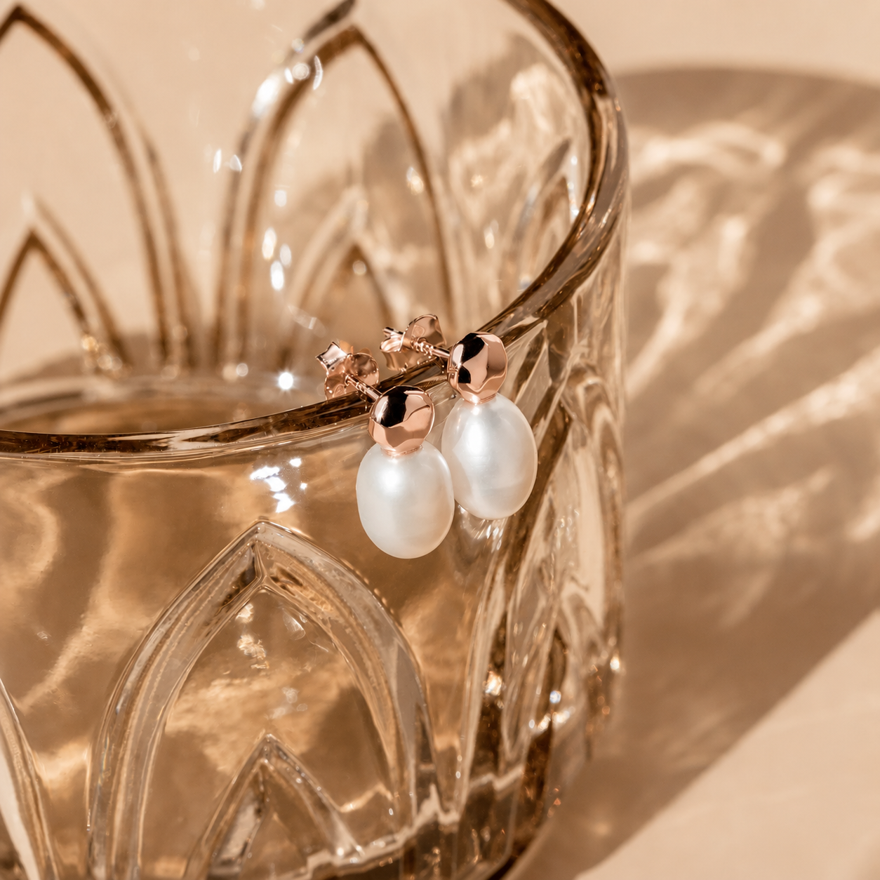 Pearl earrings with rose gold accents on a glass surface