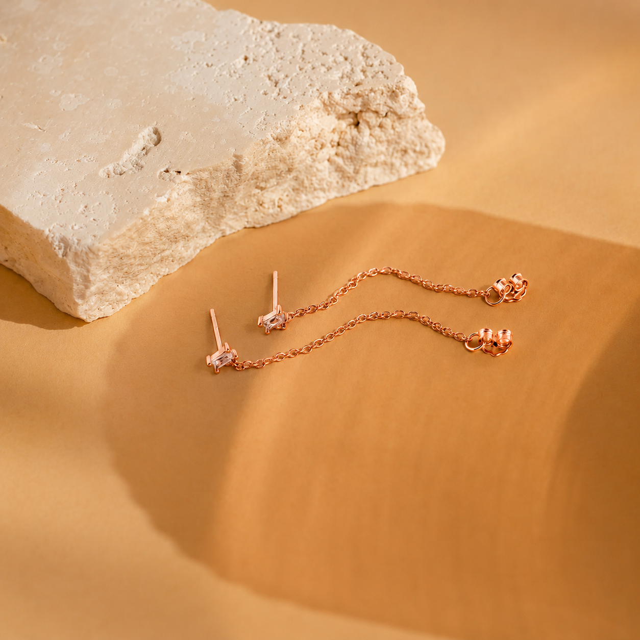 Rose gold jewelry set on a beige surface with a stone background