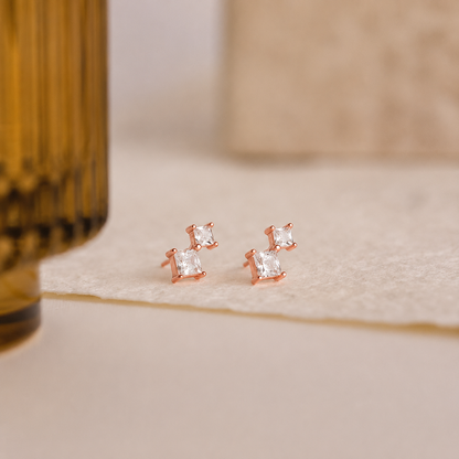 Rose gold earrings with clear gemstones on a beige surface