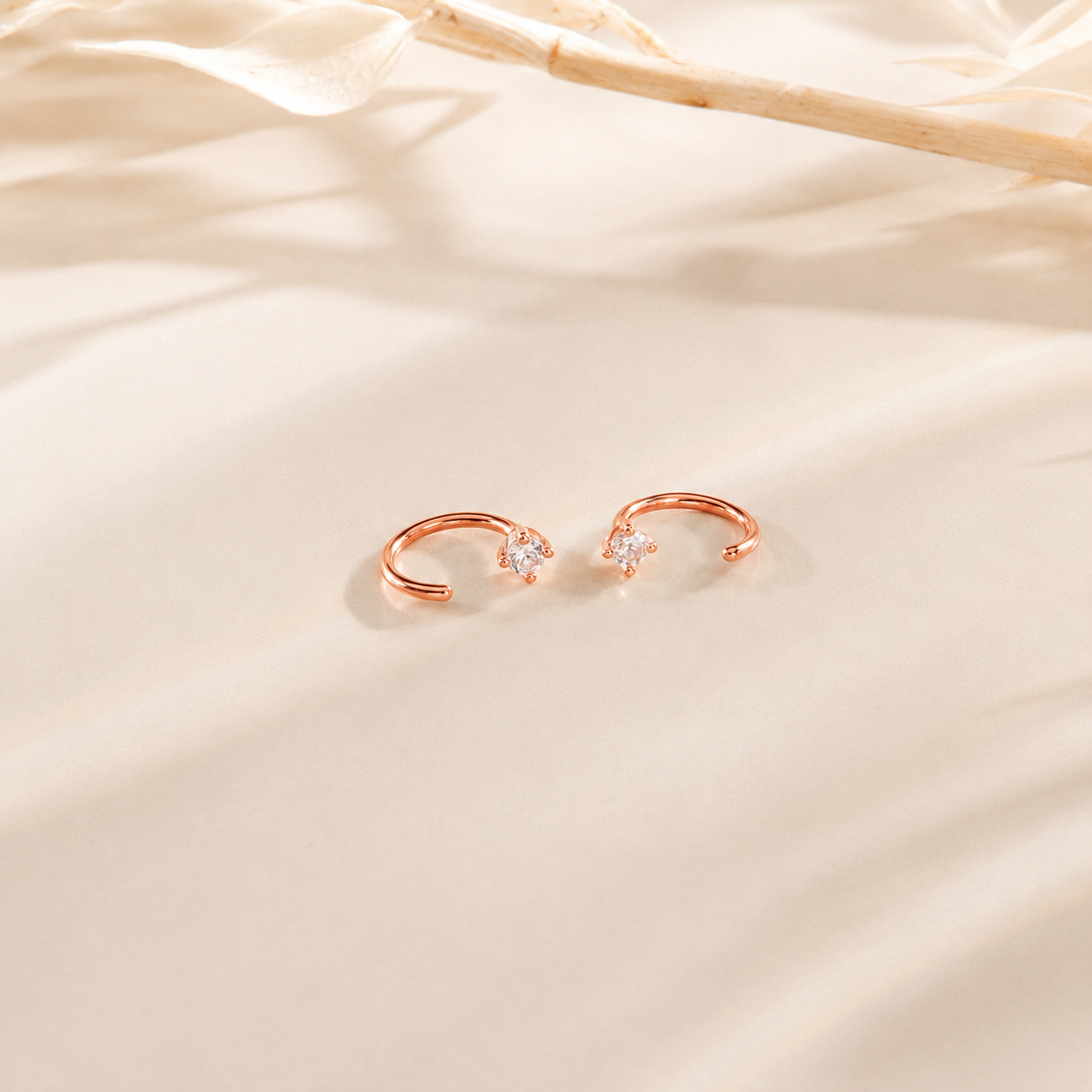 Rose gold earrings with small gemstones on a beige fabric background