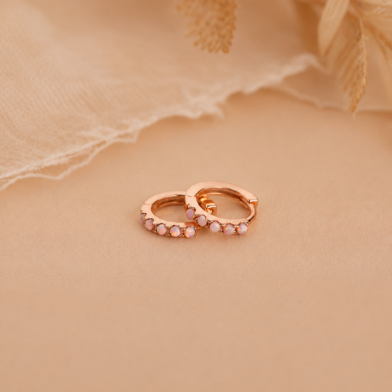 Rose gold hoop earrings with small stones on a beige fabric background