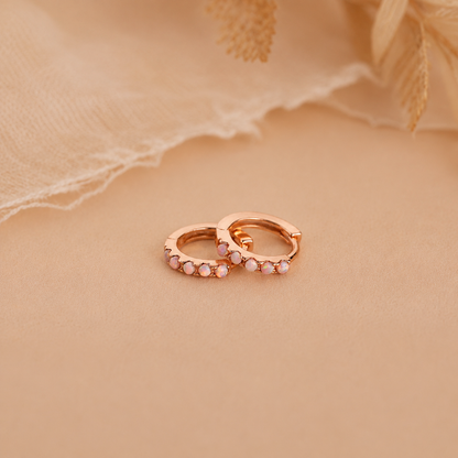 Rose gold hoop earrings with small stones on a beige fabric background
