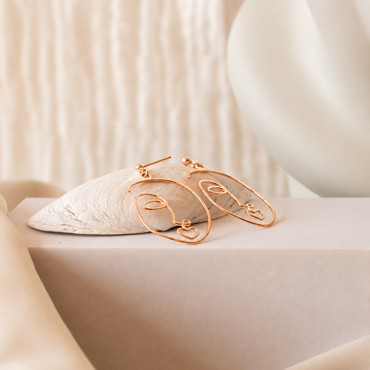 Rose Gold hoop earrings on a textured beige surface with a soft background