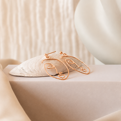 Rose Gold hoop earrings on a textured beige surface with a soft background