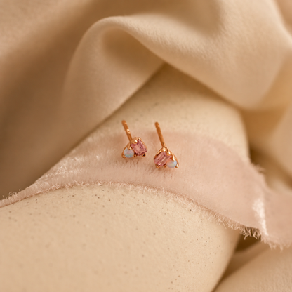Rose gold earrings with pink gemstones on a beige fabric background