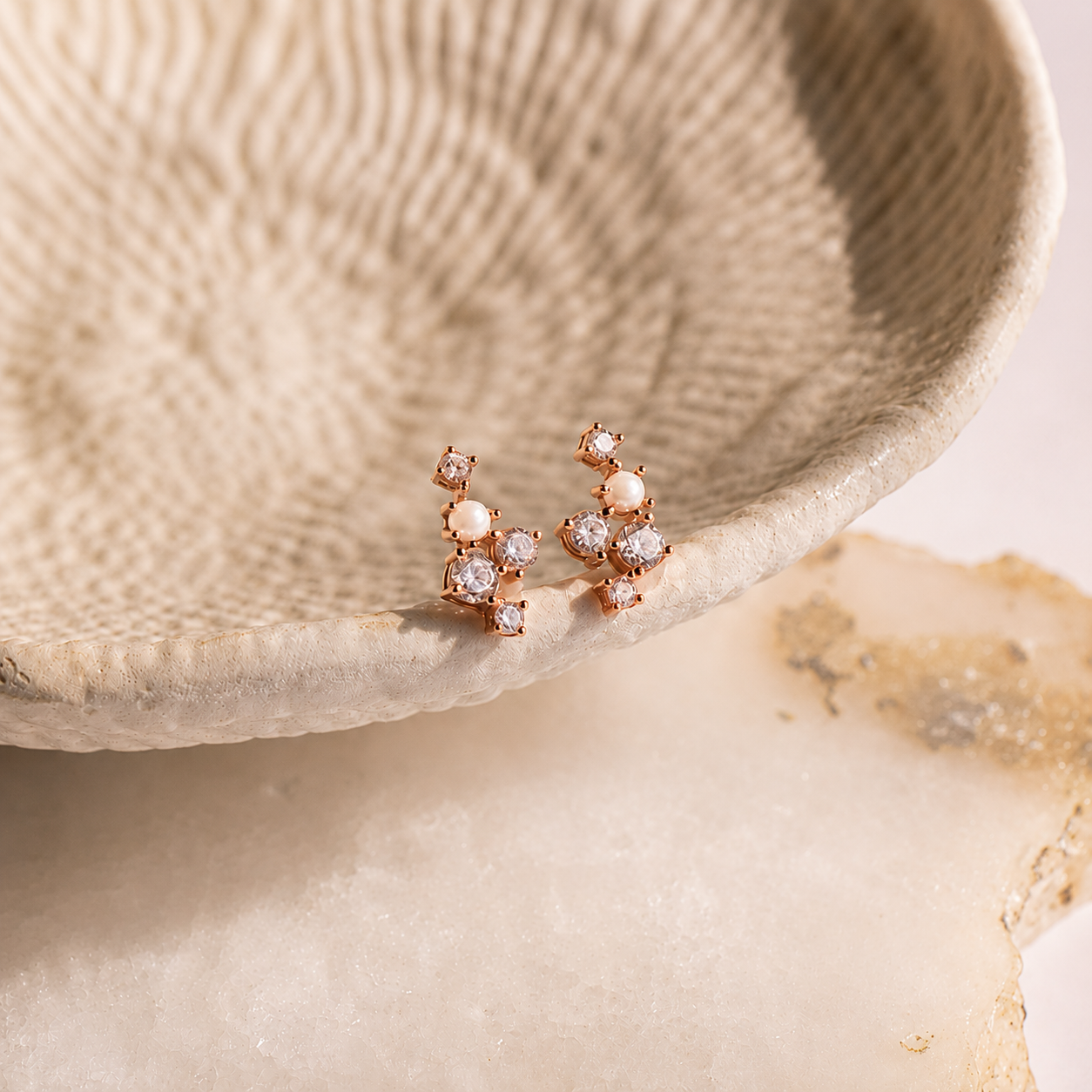 Rose gold earrings with small diamonds on a textured beige surface