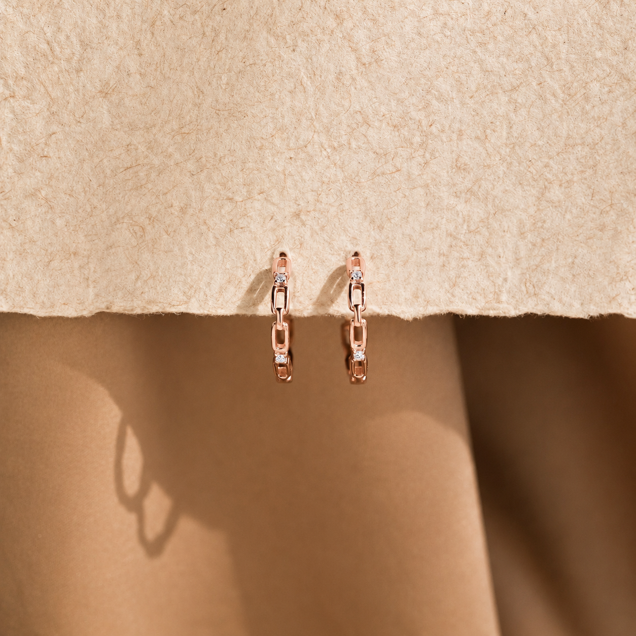 Rose gold earrings with small diamonds on a beige fabric background