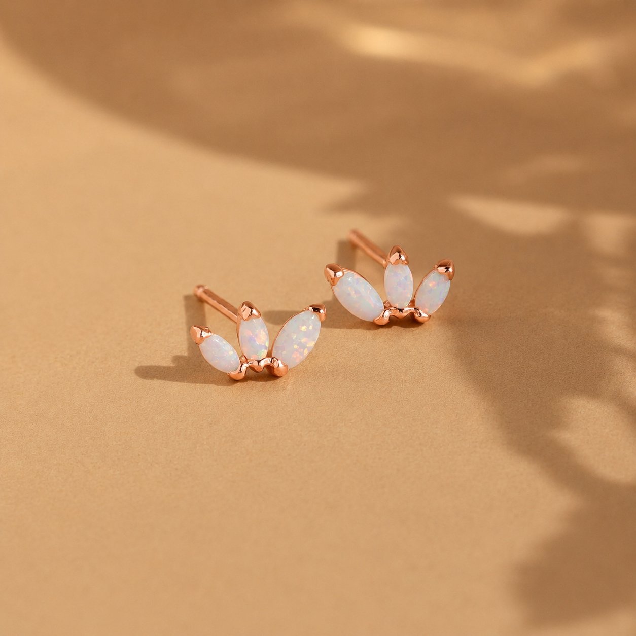 Pair of rose gold earrings with white stones on a beige background