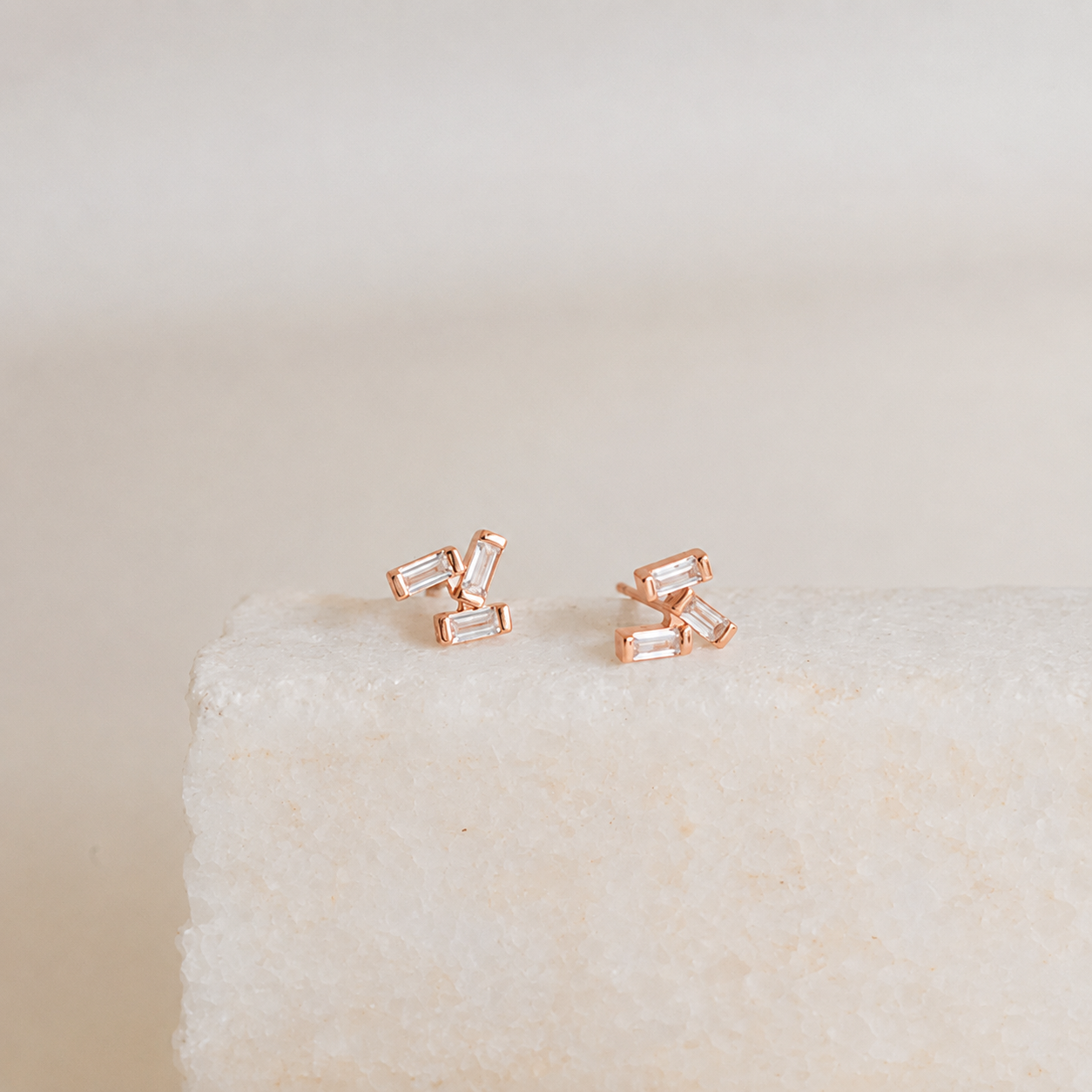 Rose gold baguette cut stud earrings on a textured beige surface