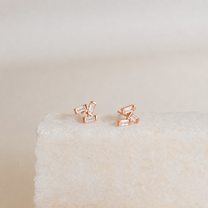 Rose gold baguette cut stud earrings on a textured beige surface