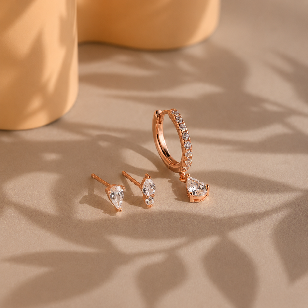 Rose gold hoop and stud earrings on a textured surface with a soft focus background