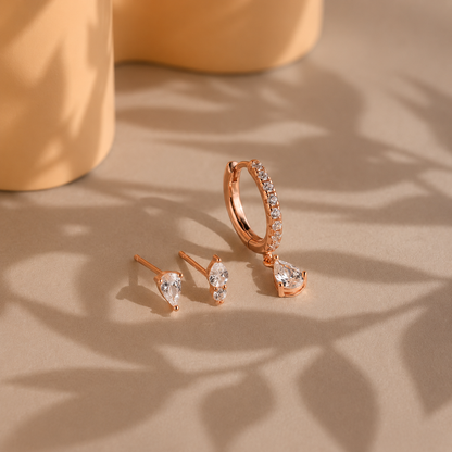 Rose gold hoop and stud earrings on a textured surface with a soft focus background