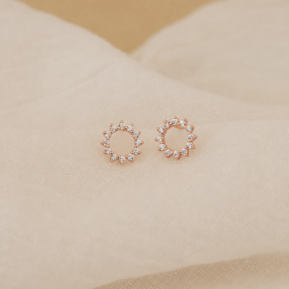 Rose gold earrings with clear stones on a beige fabric background