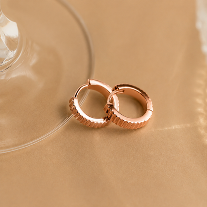 Rose gold hoop earrings on a beige background