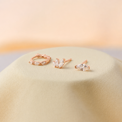 Set of rose gold earrings on a soft beige surface with a warm glow.