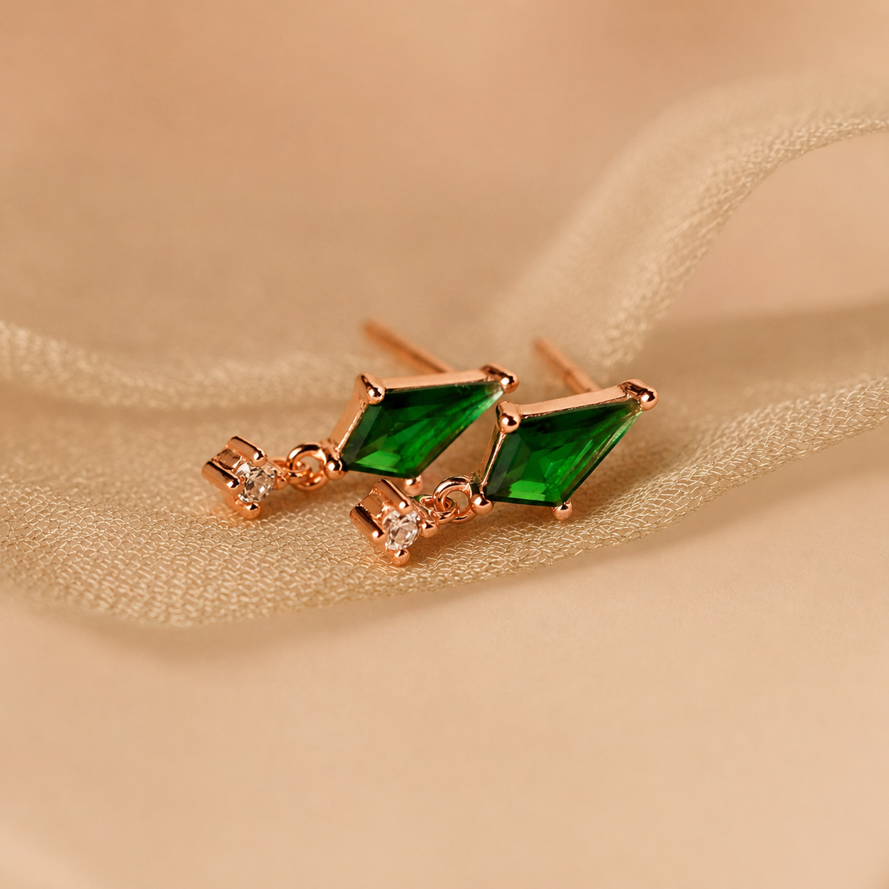 Pair of earrings with green gemstones on a beige fabric background