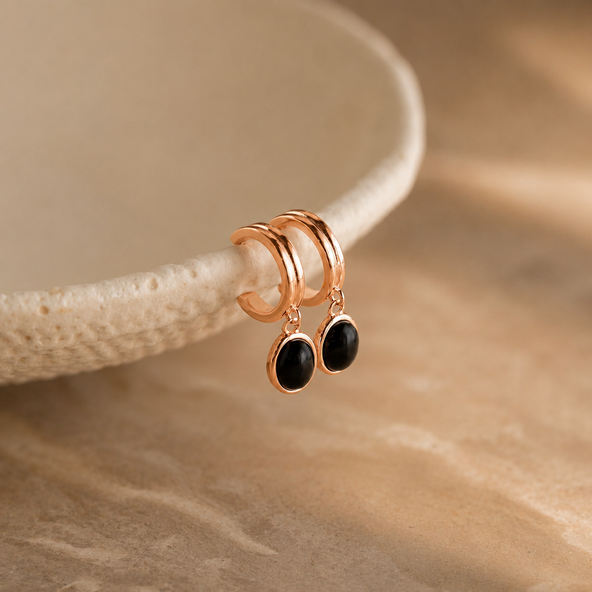 Rose gold earrings with black stones on a beige background