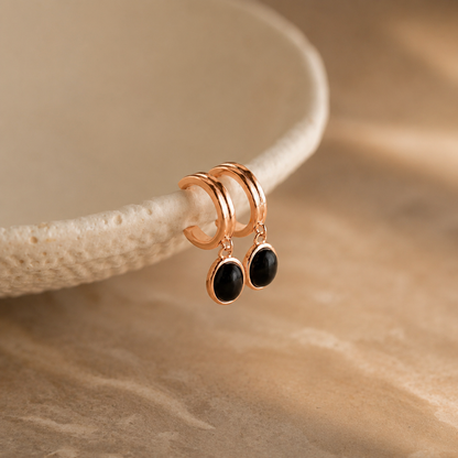 Rose gold earrings with black stones on a beige background