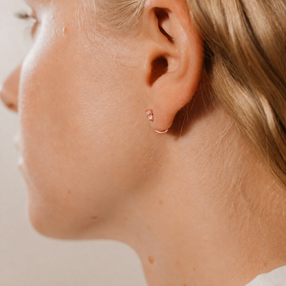 Close-up of a person wearing a small earring on a neutral background