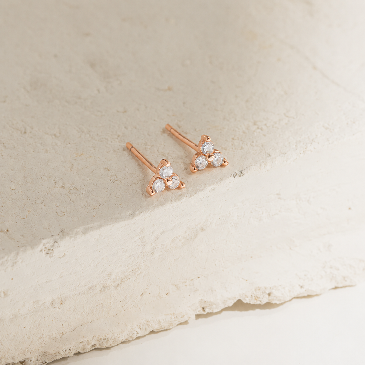 Rose gold earrings with clear gemstones on a beige stone surface