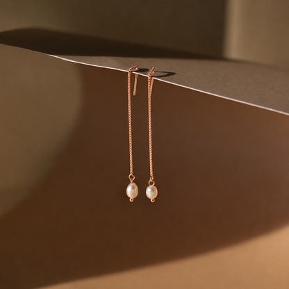 Rose gold earrings with pearl drops on a brown surface