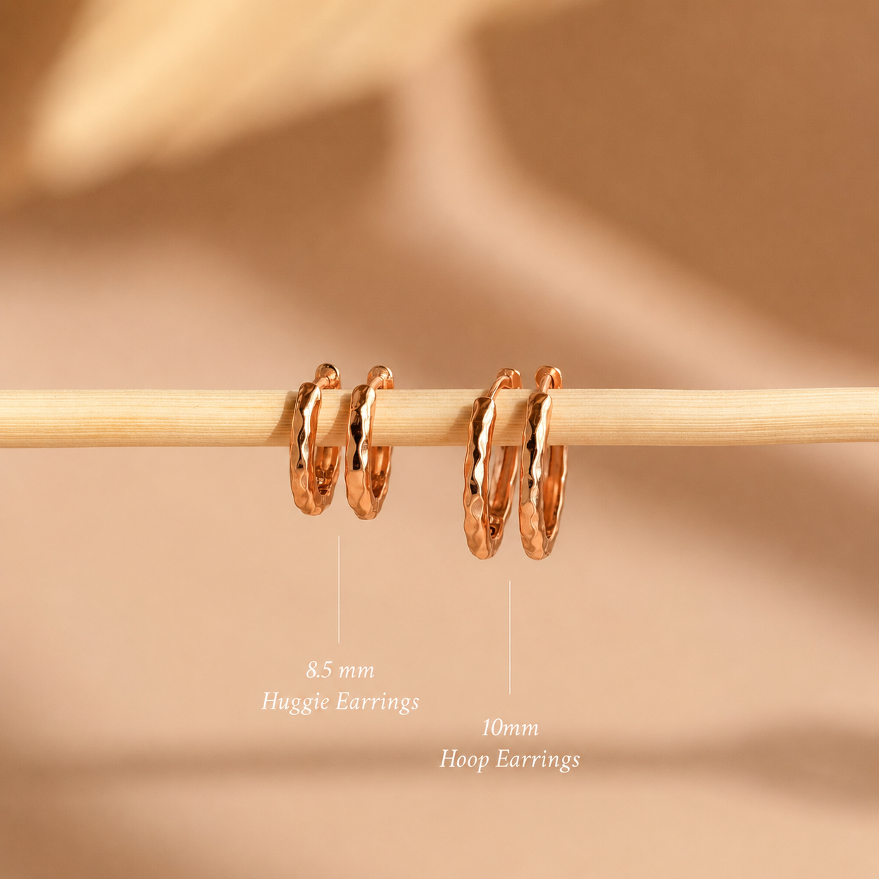 Rose gold hoop earrings on a wooden stick with size labels against a beige background