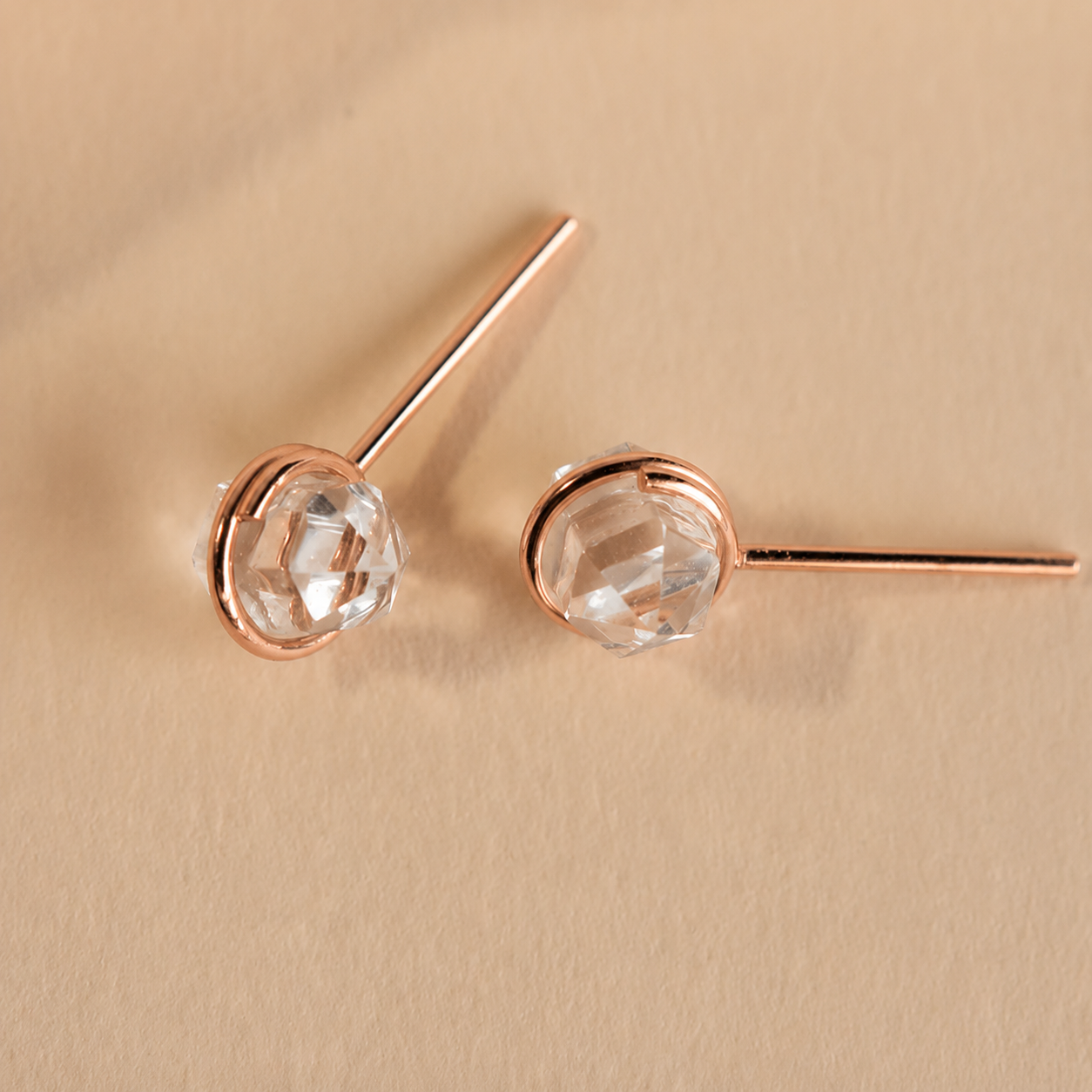 Rose gold earrings with clear gemstones on a beige background