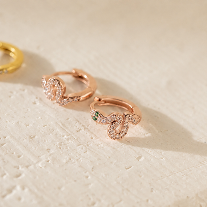 Rose gold hoop earrings with green gemstones on a textured beige surface