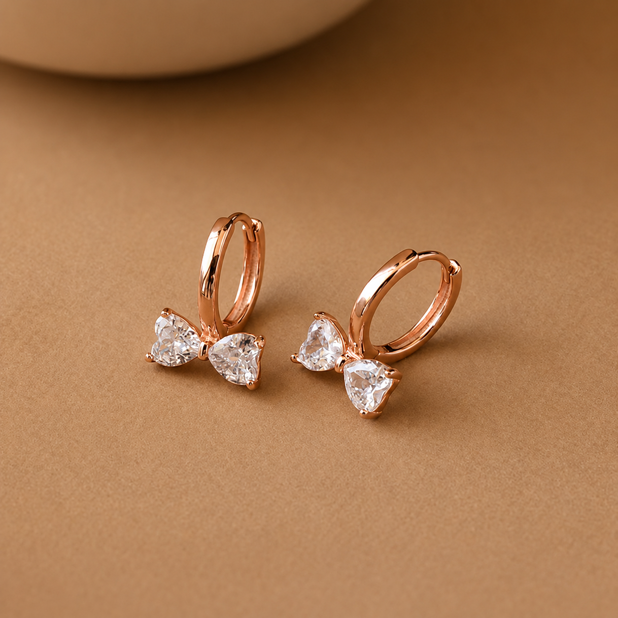 Rose gold bow-shaped earrings with clear gemstones on a brown background