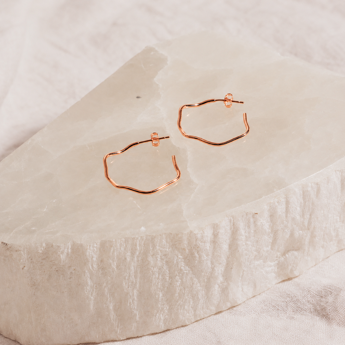Rose gold hoop earrings on a textured beige surface