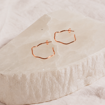 Rose gold hoop earrings on a textured beige surface