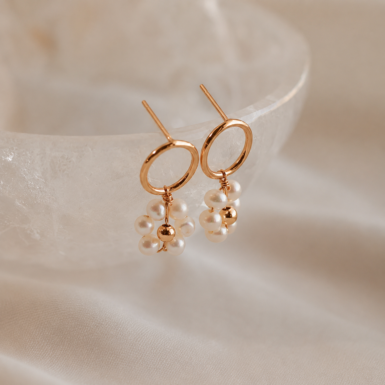 Gold earrings with pearl drops on a soft beige fabric background